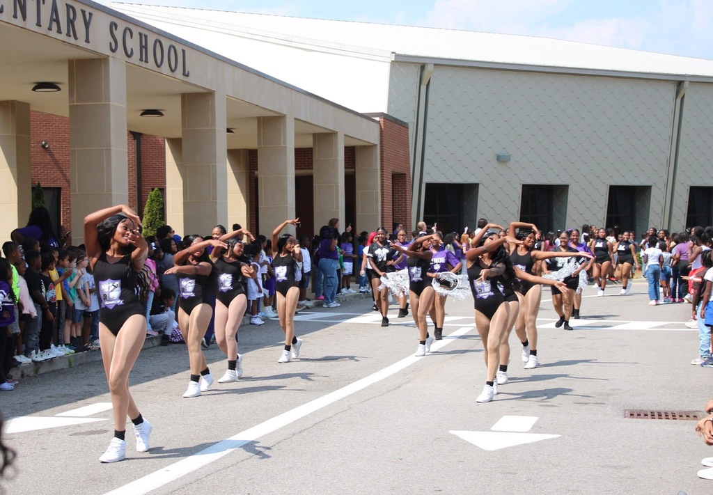A high school dance team performs on the road in front of an elementary school.