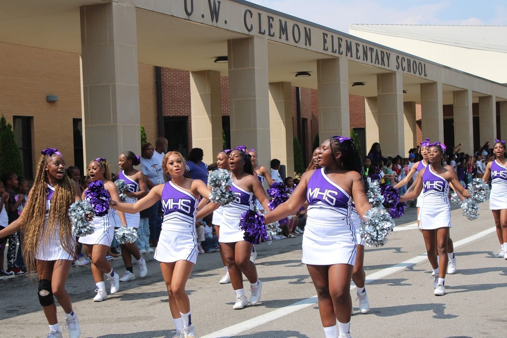 High school cheerleaders perform in front of an elementary school. 