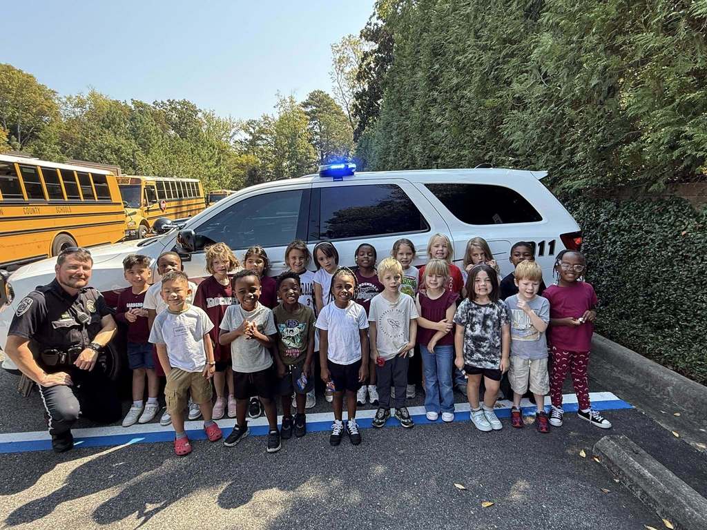 A group of kindergarten students stand in front of a police car.