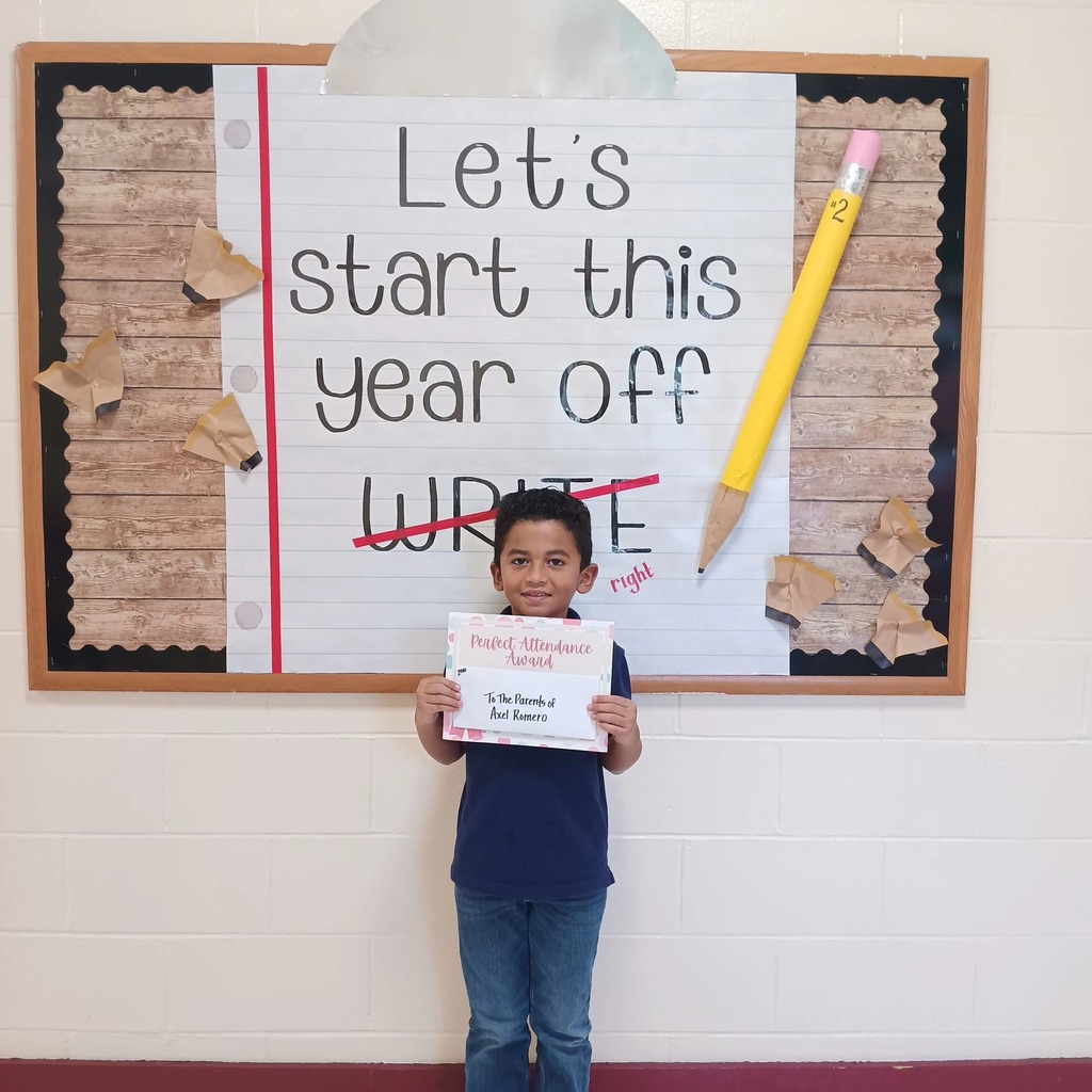 A student holds a certificate and stands in front of a sign that says "Let's start this school year off write", with write crossed out and replaced with "right."