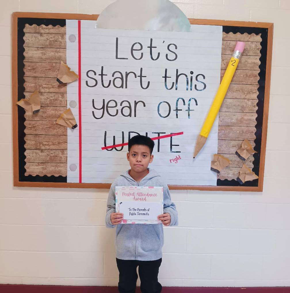 A student holds a certificate and stands in front of a sign that says "Let's start this school year off write", with write crossed out and replaced with "right."
