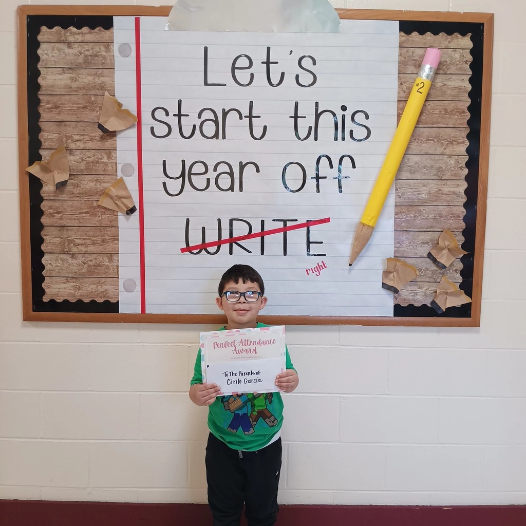 A student holds a certificate and stands in front of a sign that says "Let's start this school year off write", with write crossed out and replaced with "right."