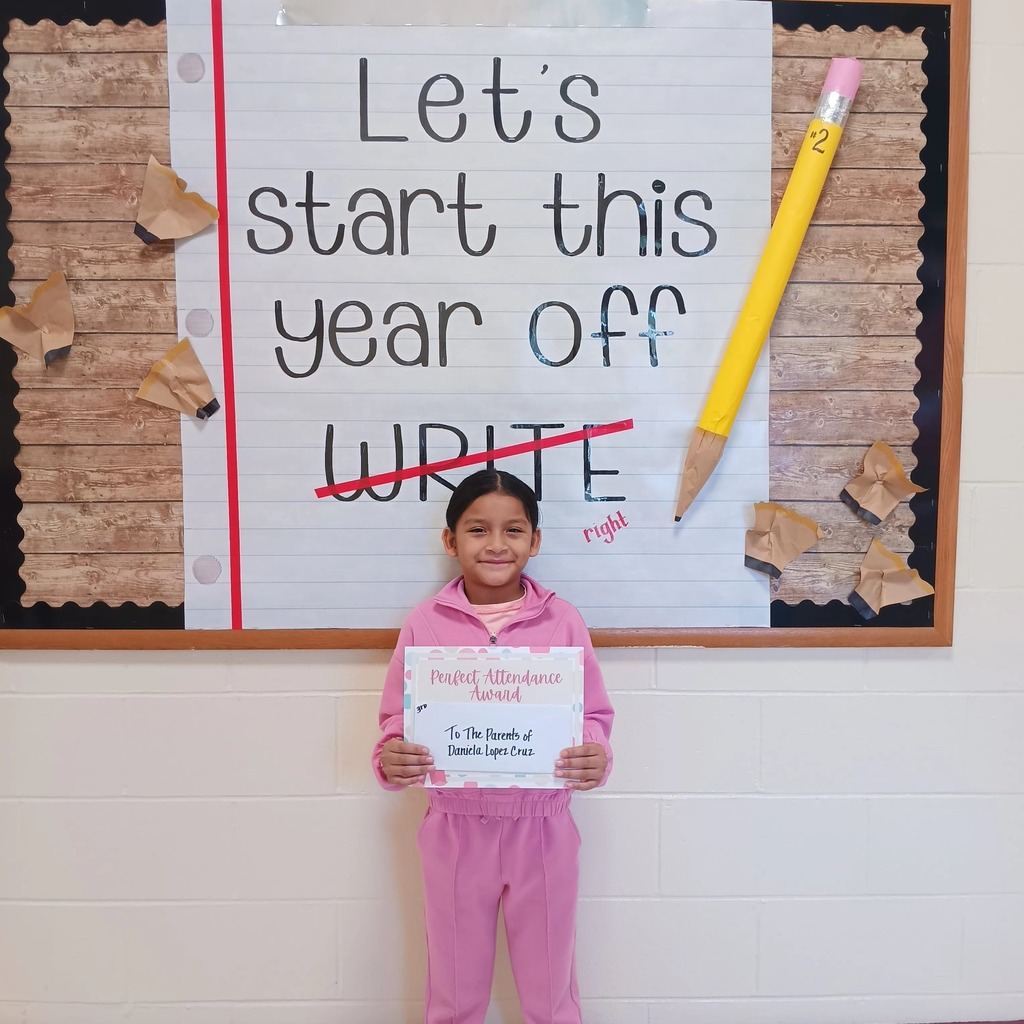A student holds a certificate and stands in front of a sign that says "Let's start this school year off write", with write crossed out and replaced with "right."