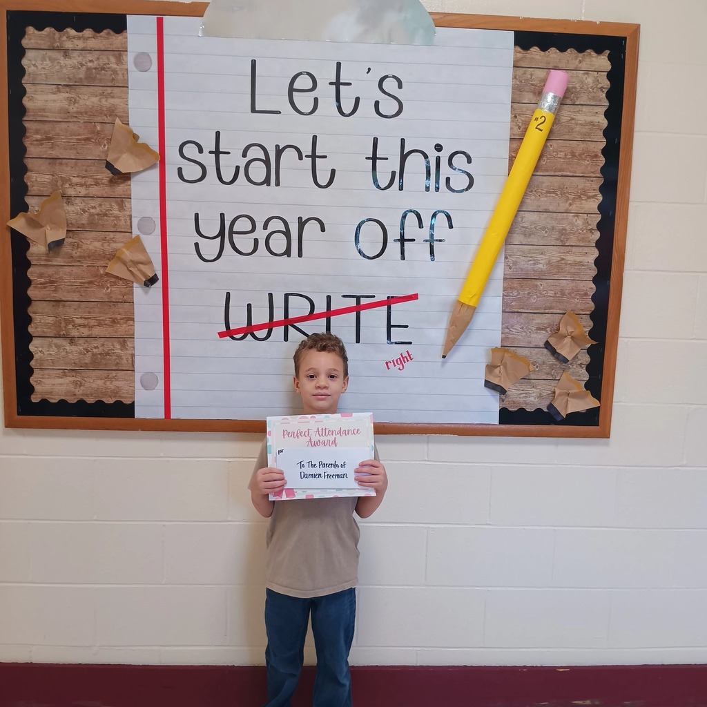 A student holds a certificate and stands in front of a sign that says "Let's start this school year off write", with write crossed out and replaced with "right."