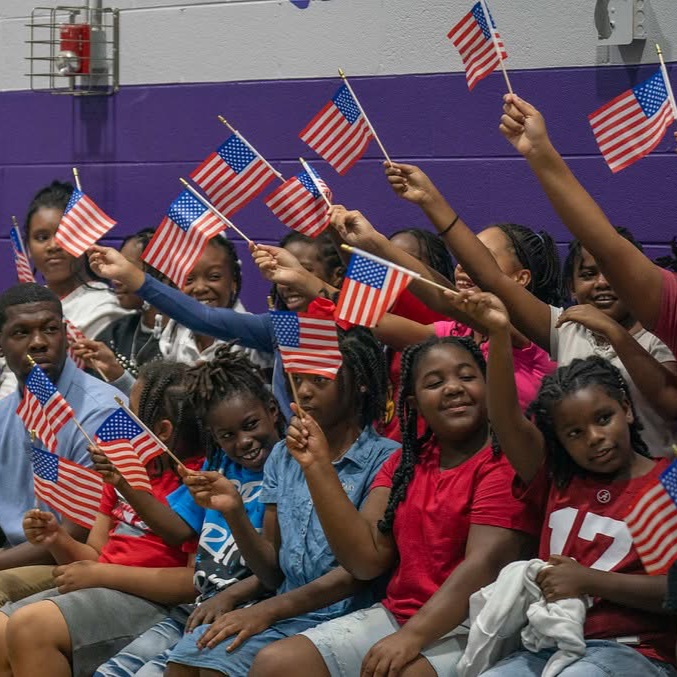 The students are waving flags as Gov. Ivey walks into the gym.