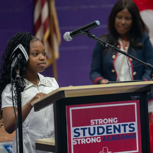 A student standing at the podium introducing Gov. Ivey.