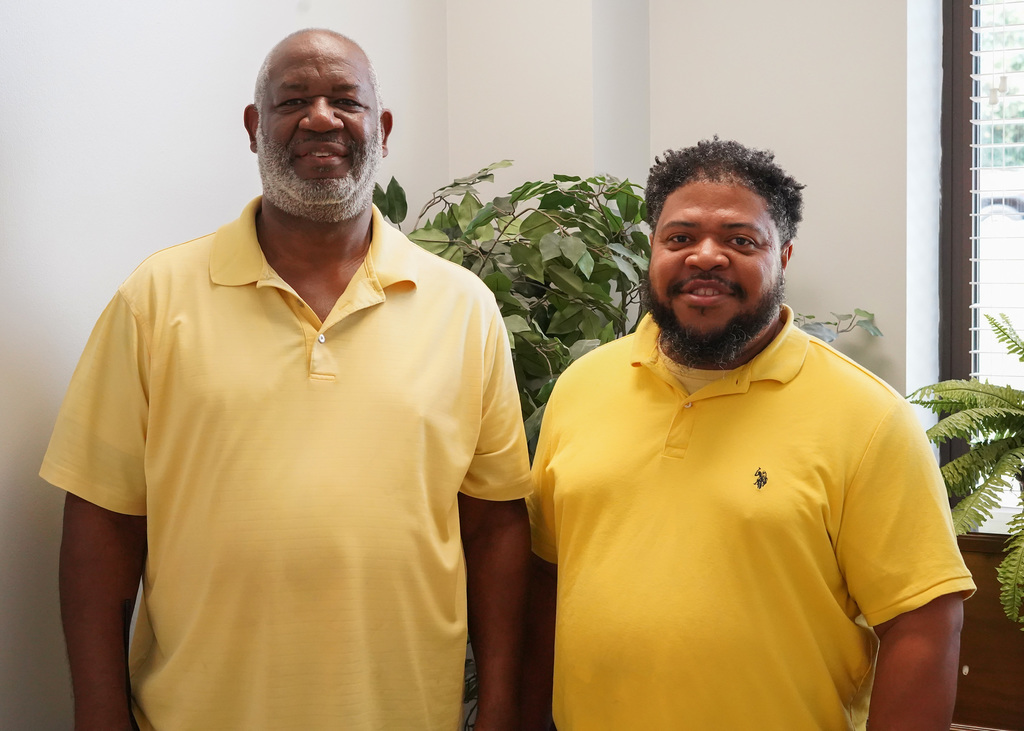 Two men stand together for a photo and smile. They’re both wearing yellow polos to show support for Childhood Cancer Awareness.