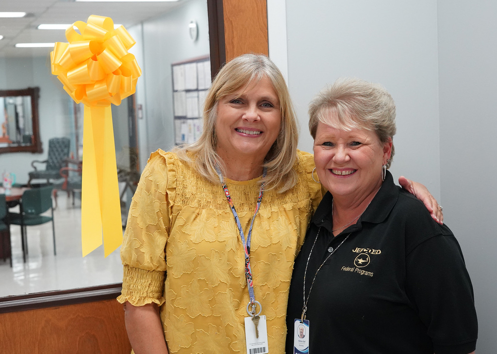 Two women stand together in a hallway and pose for a photo. They’re wearing gold to show support for Childhood Cancer Awareness.