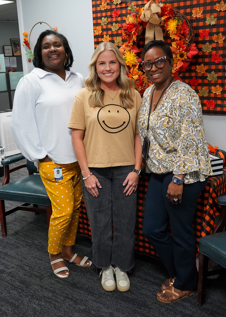 Three women stand together in a hallway and pose for a photo. They’re all wearing gold or yellow for Childhood Cancer Awareness.