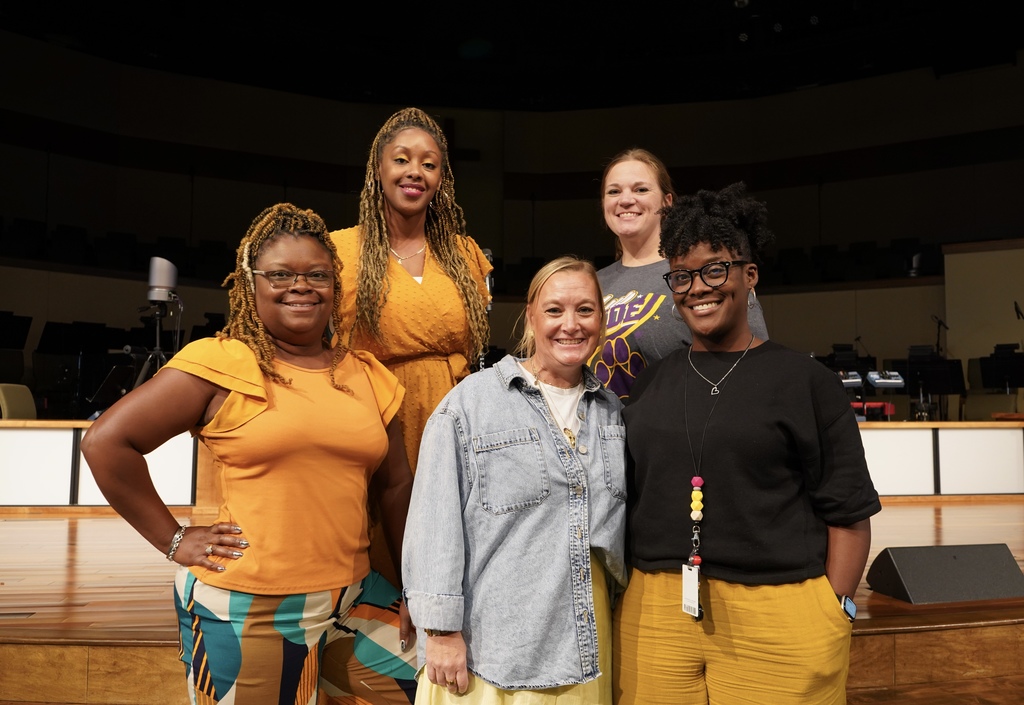 A group of people stand together and smile for a photo inside a church. They’re wearing gold and yellow to show support for Childhood Cancer Awareness.