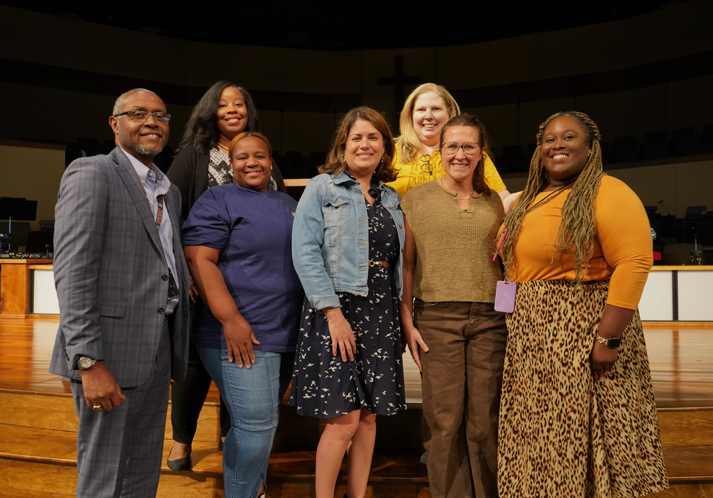 A group of people stand together and smile for a photo inside a church. They’re wearing gold and yellow to show support for Childhood Cancer Awareness.