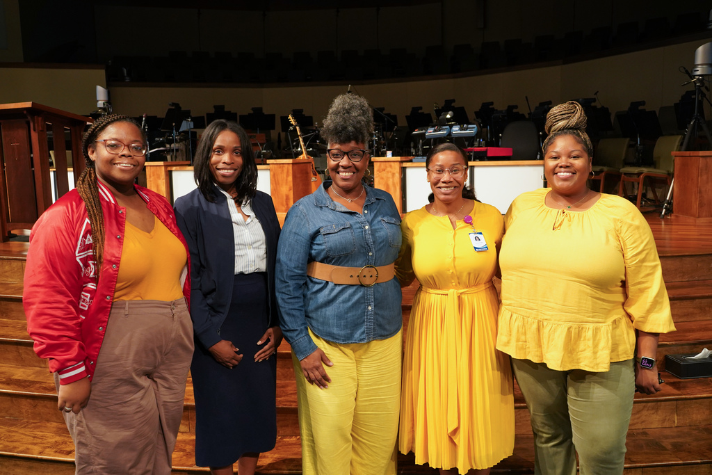 A group of people stand together and smile for a photo inside a church. They’re wearing gold and yellow to show support for Childhood Cancer Awareness.