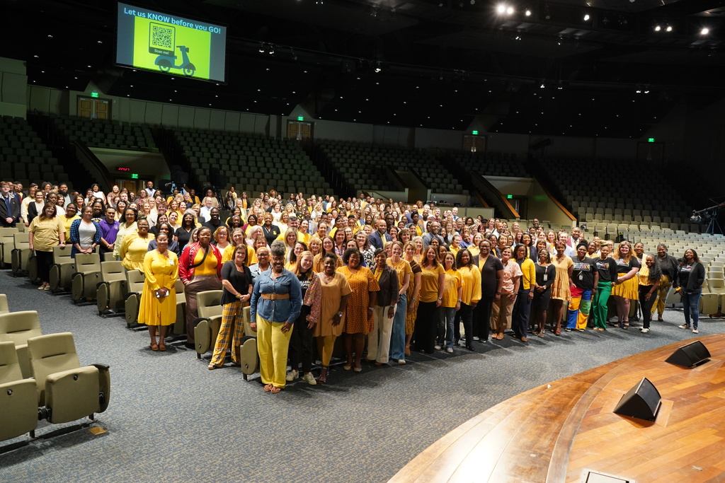 A large group of people stand together and smile for a photo inside a church. They’re wearing gold and yellow to show support for Childhood Cancer Awareness.