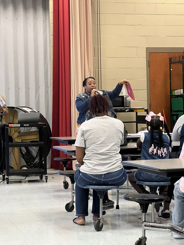 A woman gives a presentation in front of families inside a school building.
