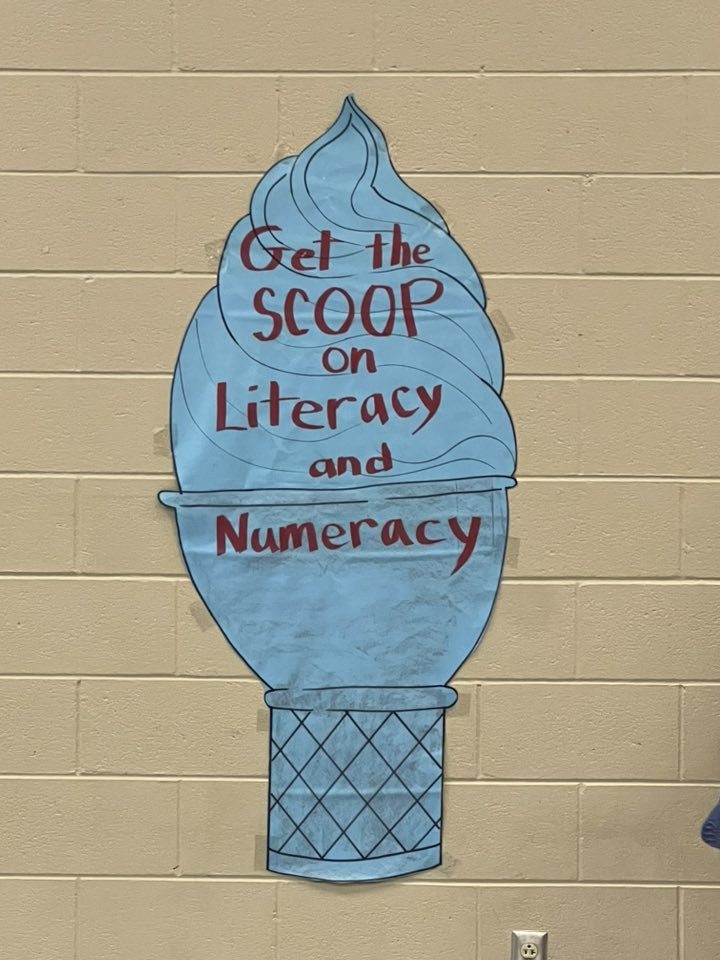 The photo is of large paper in the shape of an ice cream cone taped to a wall. A message written in marker reads "Get the Scoop on Literacy and Numeracy."