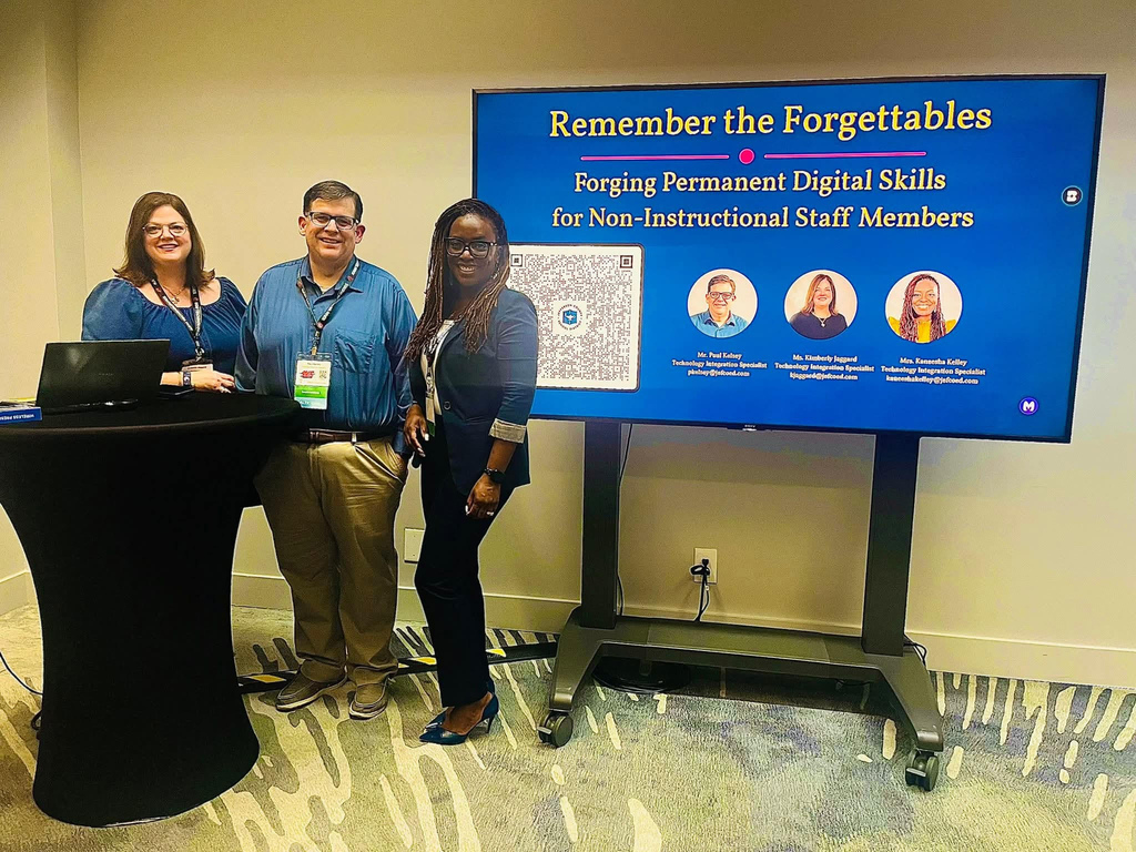 Three people smile while standing between a podium and a screen with a presentation on it. The screen says" Remember the Forgettables Forging Permanent Digital Skills for Non-Intructional Staff Members." The text is above photos of the three presenters.