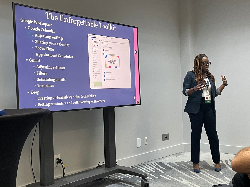 A woman stands in the front of a room, giving a presentation.