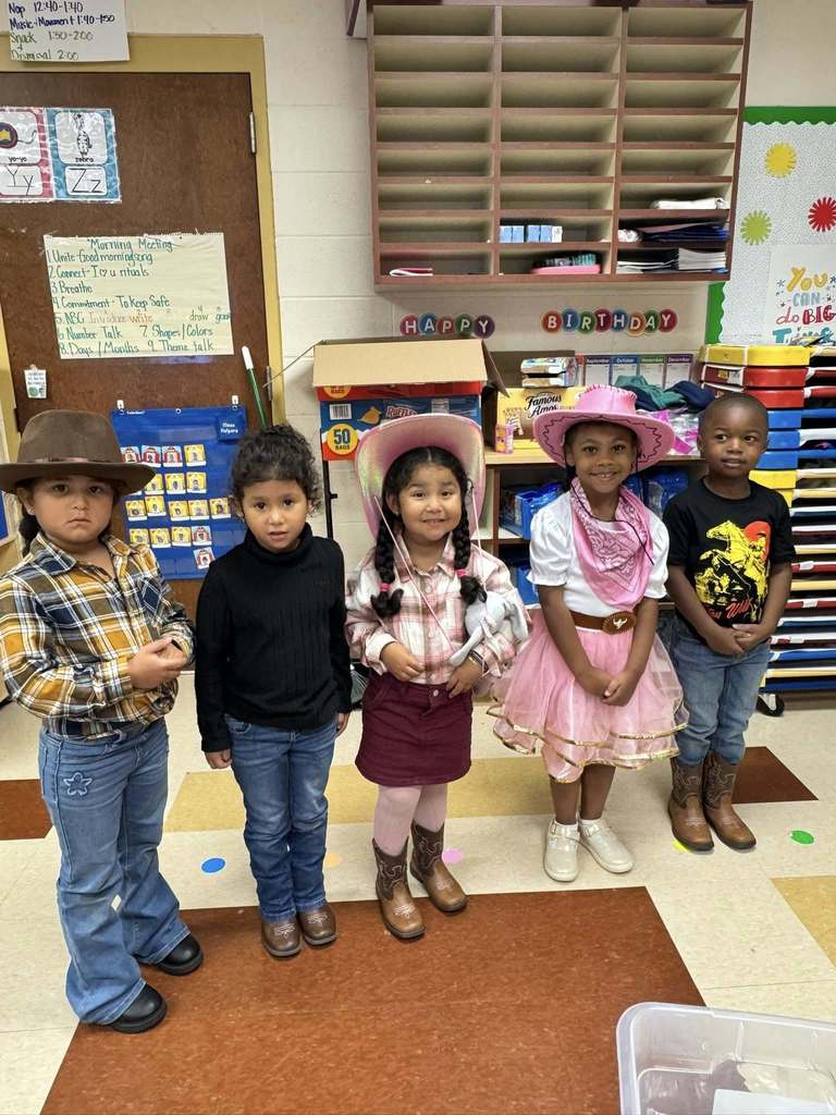 Students wearing vaquero inspired outfits stand in a classroom and smile.