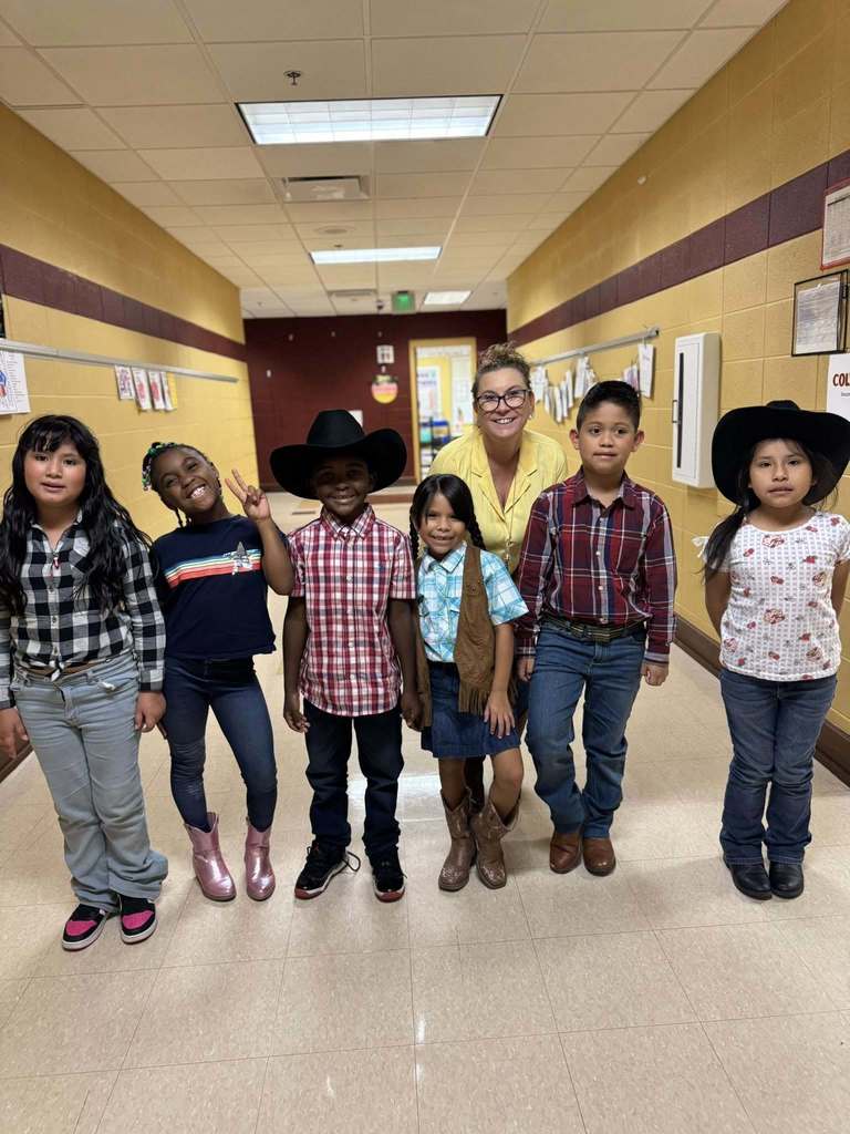Students and a teacher wearing vaquero inspired outfits stand in a school hallway and smile.