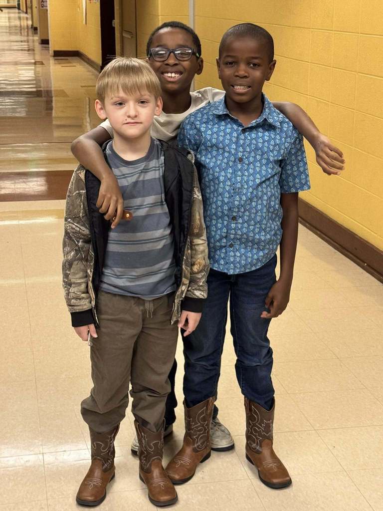 Students wearing vaquero inspired outfits stand in a school hallway and smile.