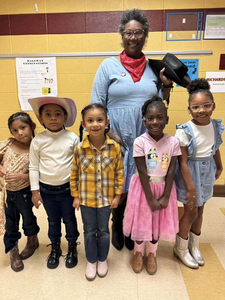 Students and a teacher wearing vaquero inspired outfits stand in a school hallway and smile.