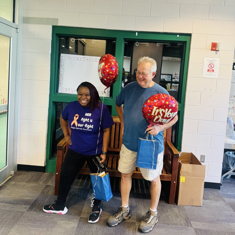 Mr. Rick and Ms. Shawanda holding a balloon and gift bag from the school employees thanking them for being such great custodians on School Custodian Day.
