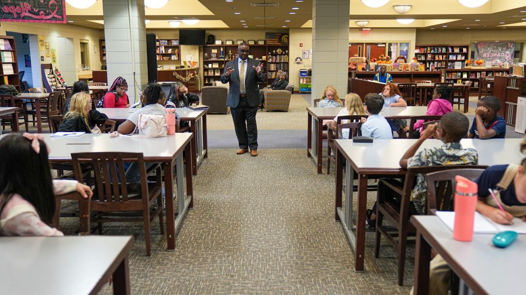 JEFCOED Superintendent Dr. Gonsoulin stands in a library and talks to students. The students are sitting at tables. 