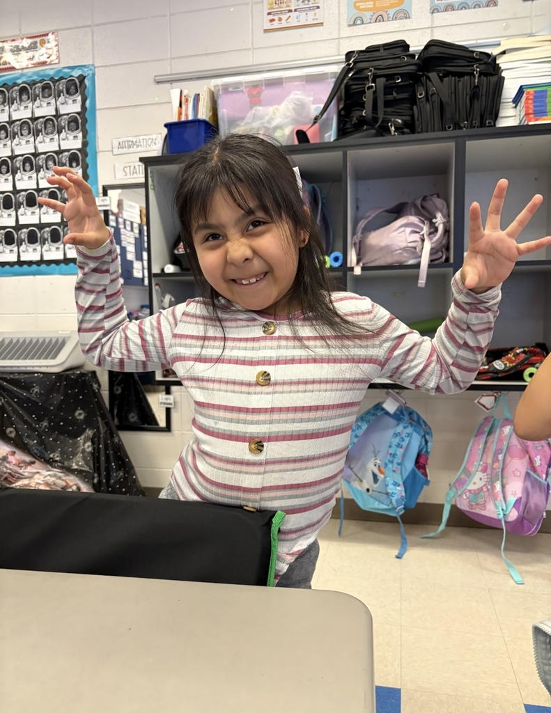 A student stands in a classroom, holding her arms out.