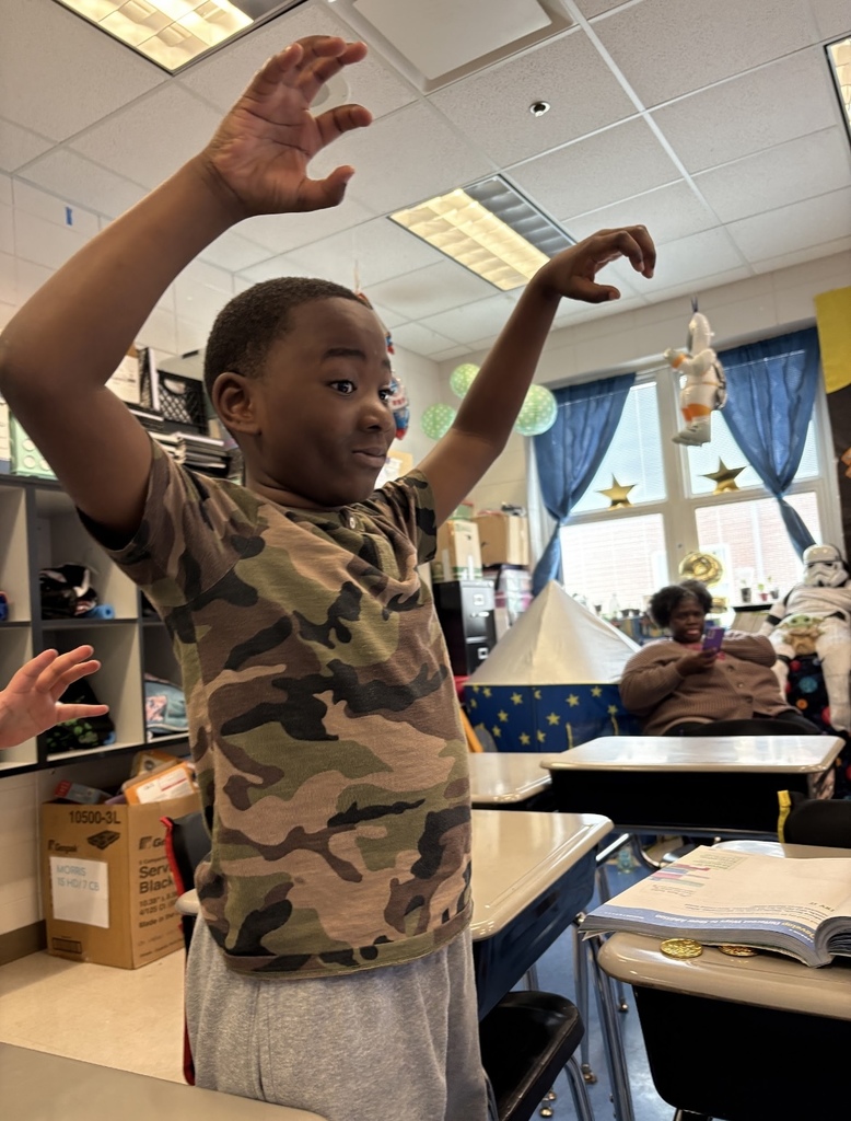 A student stands in a classroom and holds his arms up.