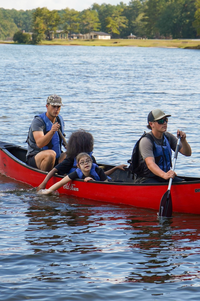 Four people sit in a canoe on a lake. Two of them sit in the middle, putting their hands in the water.
