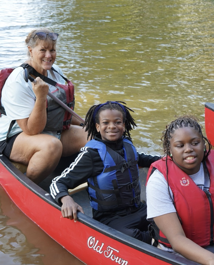 Students and an adult sit in a canoe and smile.