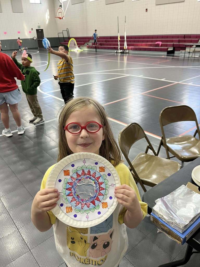 A student stands in a school gym and smiles while holding a hand-made Mexican mirror.