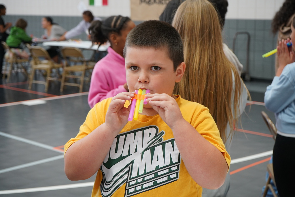 A student stands in a school gym and plays a hand-made pan flute.