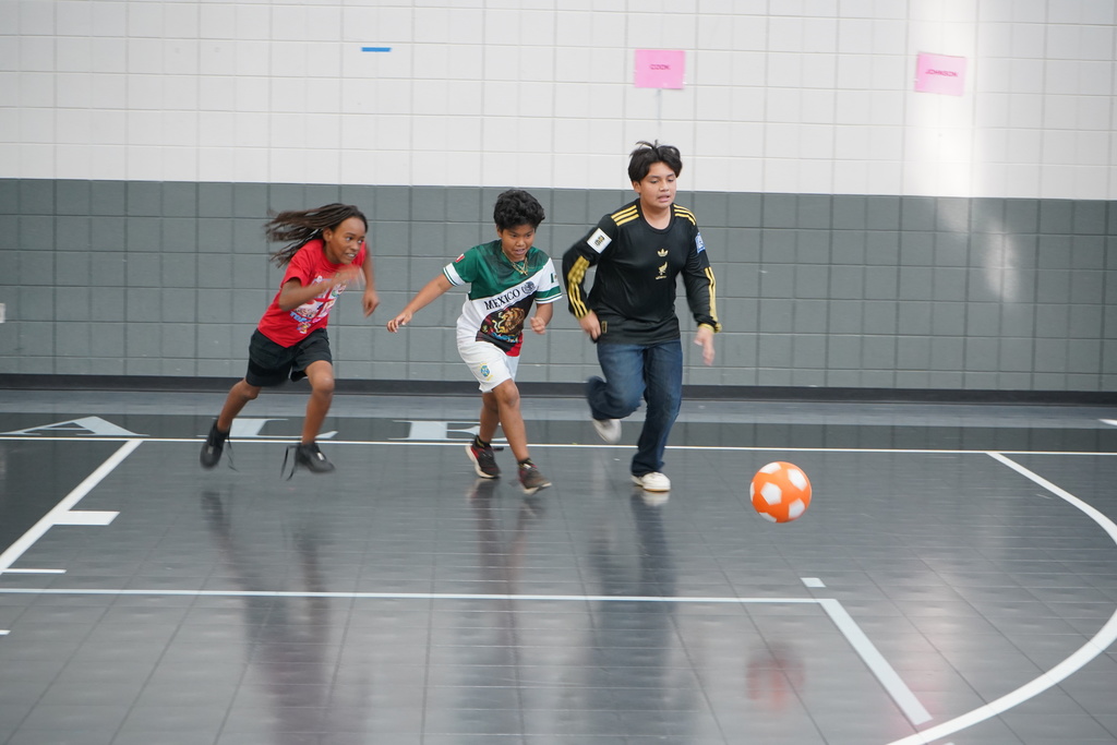 Students play soccer in a school gym.