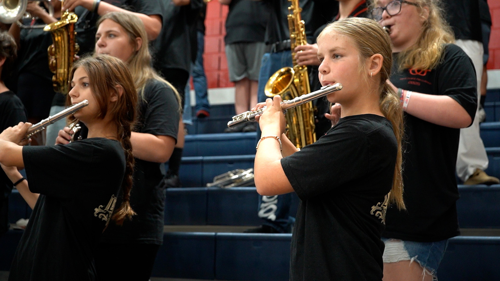 Students in a marching band play instruments in a school gym.