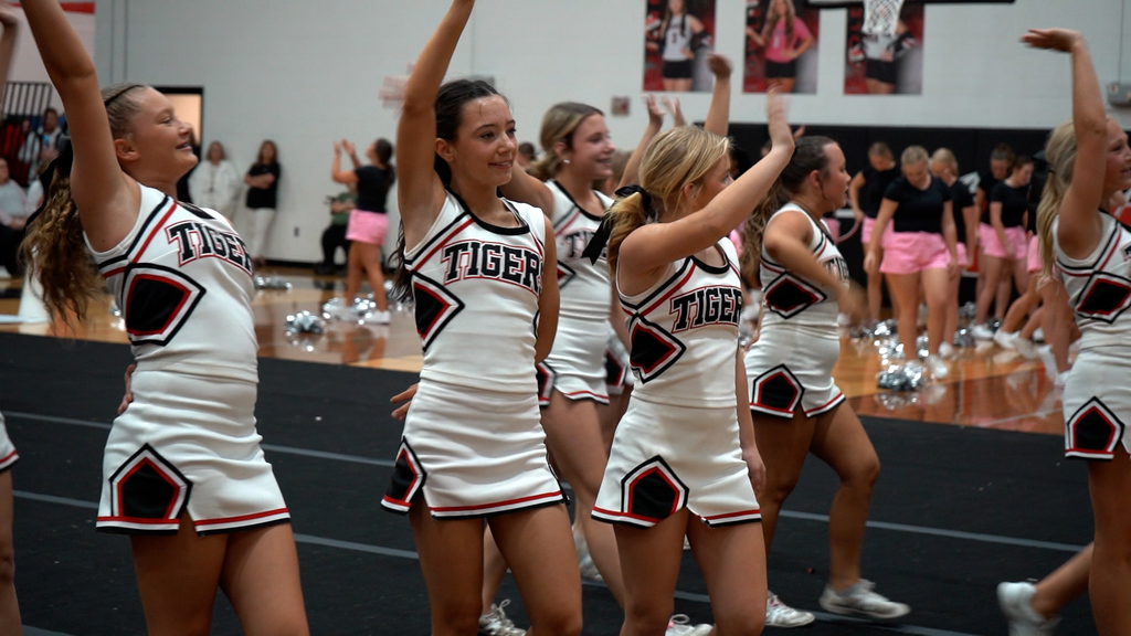 Cheerleaders wave while performing in a school gym.