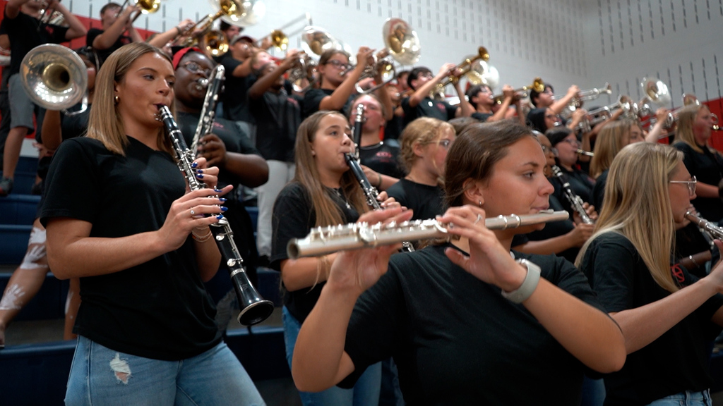 Students in a band stand on bleachers and play instruments.