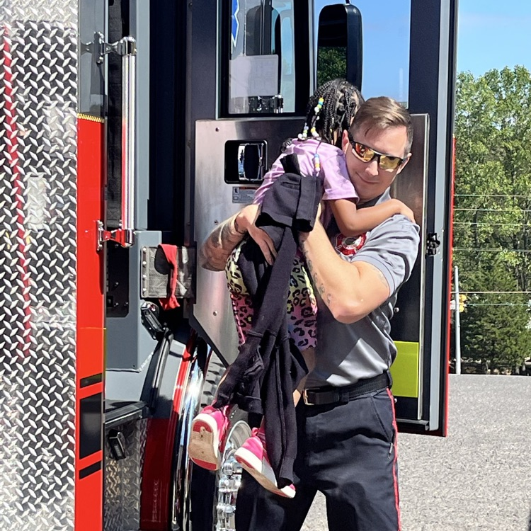 A fire fighter helping a student get out of the fire truck.
