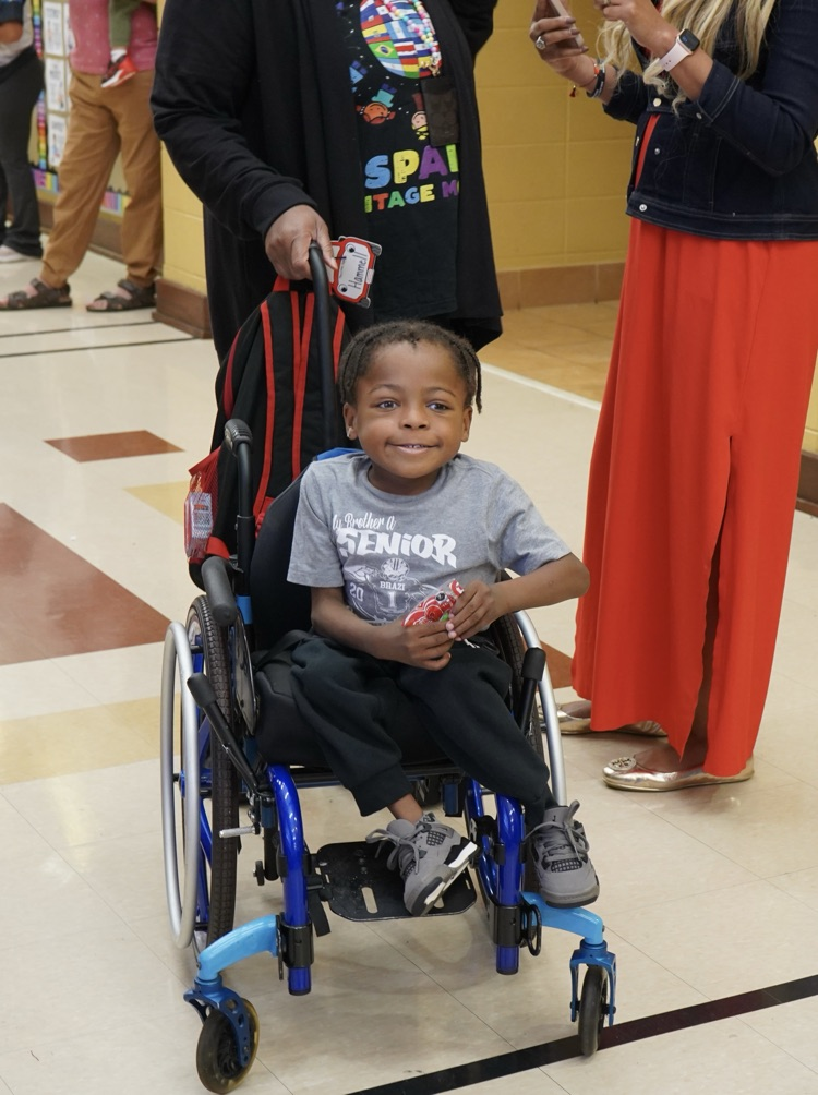 A little boy holds candy while an adult pushes him in a wheelchair