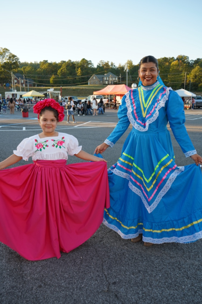 A girl and a woman stand together for a photo at a festival held in a school parking lot