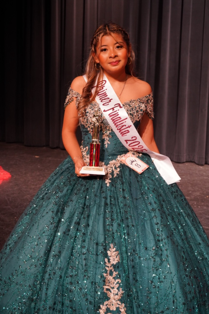 A girl wearing a green Quinceañera dress holds a trophy and smiles.
