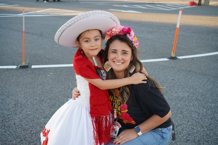 A student and a teacher stand together and smile while at a Hispanic Heritage Month festival.