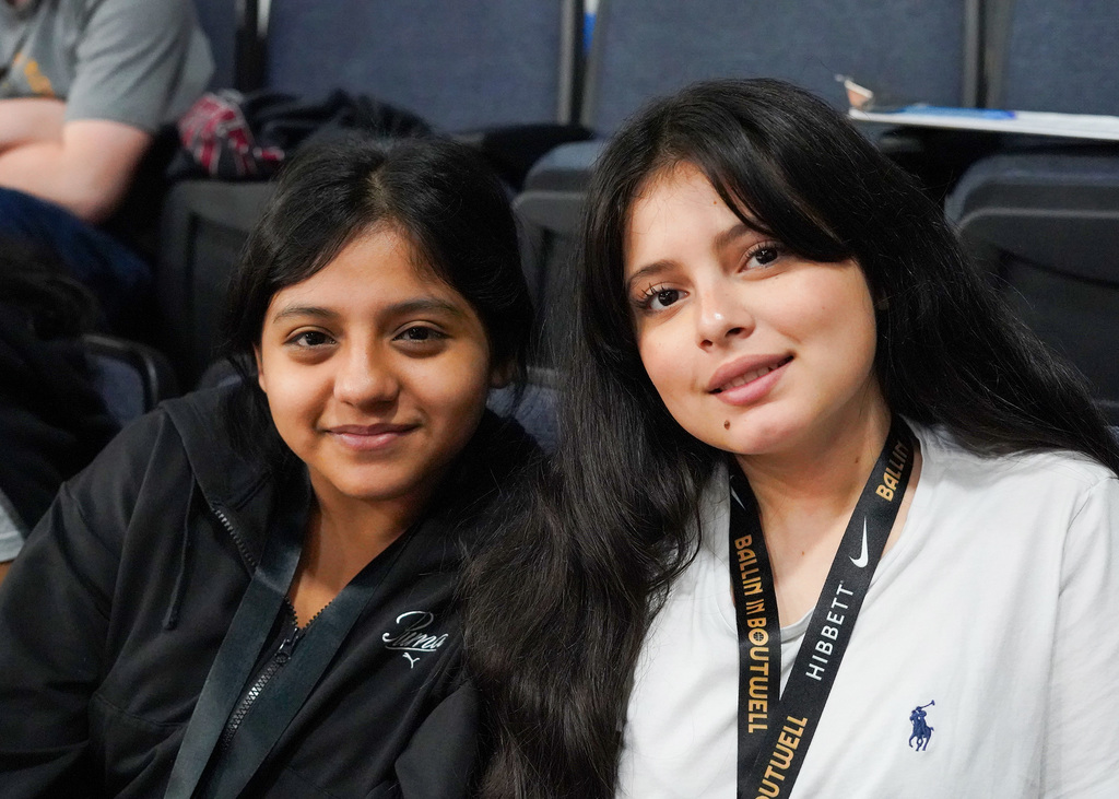 Two female students smile for the camera during a basketball game.