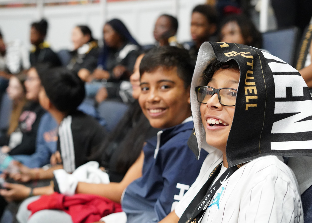 Two students look on as they attend a basketball game at Boutwell Auditorum. They are smiling and one is wearing a towel over his head.