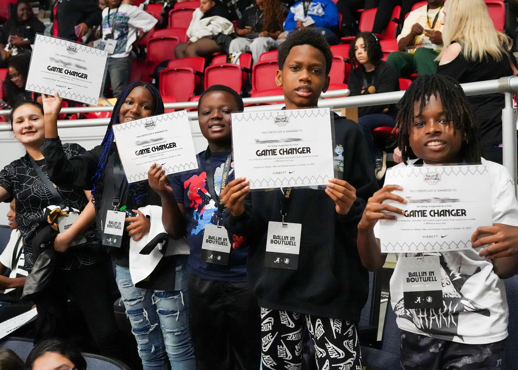 Students are attending a basketball game as a reward. They are holding up certificates that recognize them as Game Changers.