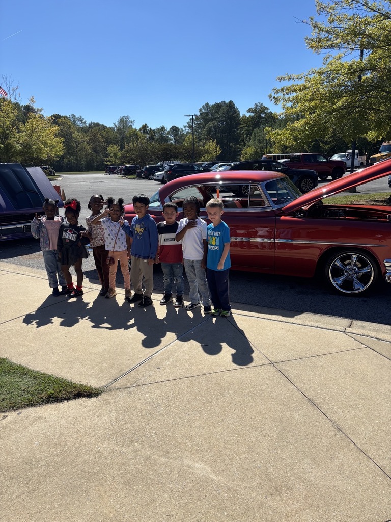 Students stand in front of a vintage car and smile.