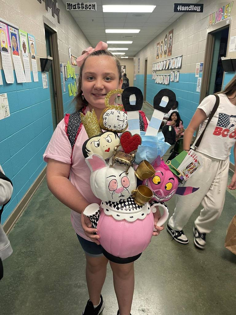 A student holds a pumpkin decorated in the theme of Alice In Wonderland.