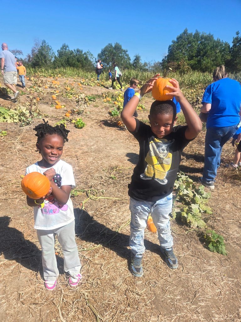 Two students stand in a pumpkin patch and hold pumpkins.