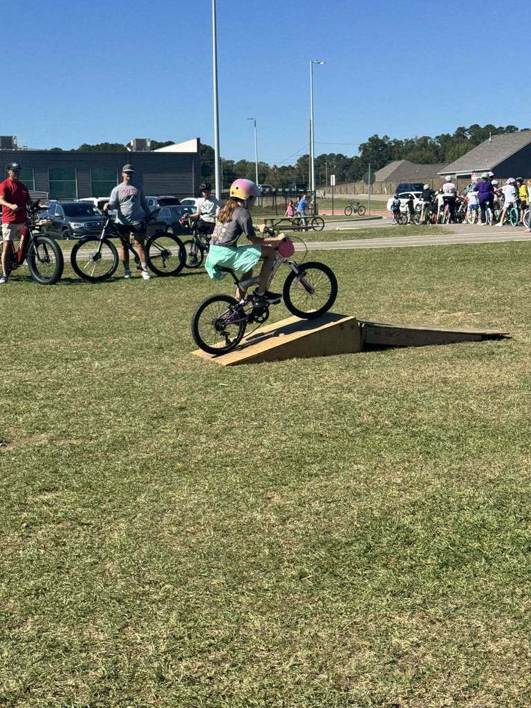A student rides a bike over a ramp in a grassy field.