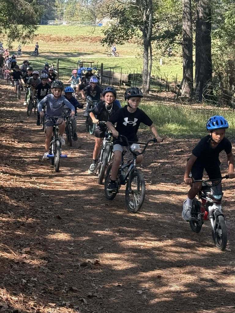 Students ride bicycles through a wooded area.